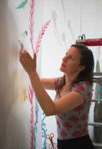 CARSON REEHER | HERALD MacKay carefully glues coral pieces into place on her large-scale art piece. She wears scissors around her neck so they don’t get lost in her piles of carefully cut paper art.