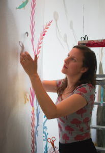 CARSON REEHER | HERALD MacKay carefully glues coral pieces into place on her large-scale art piece. She wears scissors around her neck so they don’t get lost in her piles of carefully cut paper art. 