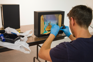 CARSON REEHER | HERALD Elly’s husband, Simon, helps her construct stages and boxes for her art. Prior to the art opening, he could be found arranging hand-made light boxes, which showcase Elly’s small worlds. 