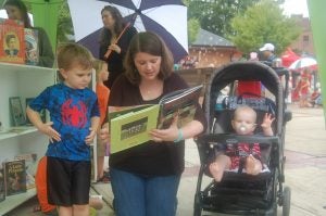 MARTIN L. CAHN | HERALD Lyndsie Blakely reads to her son, Noah, as her other son, Jeremia, waves to the camera during the All-American Downtown Celebration in Farmville on Saturday.