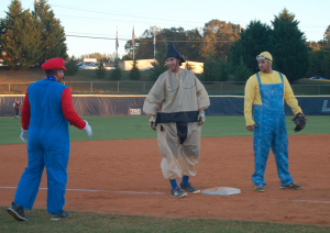 MARTIN L. CAHN | HERALD Super Mario (Assistant Coach Chad Oxendine), left, speaks to Sumo Wrestler (senior infielder Brandon Harvell), who just made it to third base as a Minion (junior right hand pitcher Tyler Wirsu) guards the position.