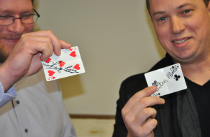 JORDAN MILES | HERALD Crews, right, holds up a card that Herald Sports Editor Titus Mohler, left, placed in his mouth. Crews switched the cards, though both Mohler and Crews held their respectively signed cards in their mouths.